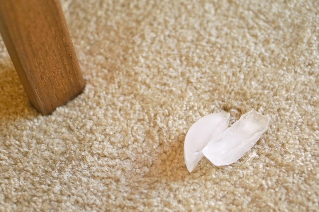 A dent in beige carpet caused by a wooden table leg. There are two ice cubes placed on the dent.