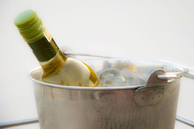 A bottle of white wine in a stainless steel ice bucket filled with ice cubes and water. The shot is a close-up showing only the top third of the ice bucket.