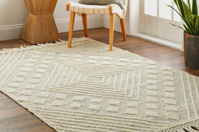 A hand-woven wool area rug in an off-white color with a raised, geometric pattern on it. Two legs of a chair are sitting on the rug.