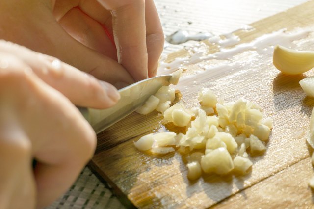 Close-up shot of a person's hands cutting garlic on a wooden cutting board with a paring knife.