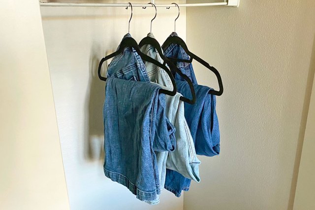 Three pairs of jeans hung up in a closet according to the hack described in this article. The jeans are hung on black velvet hangers.