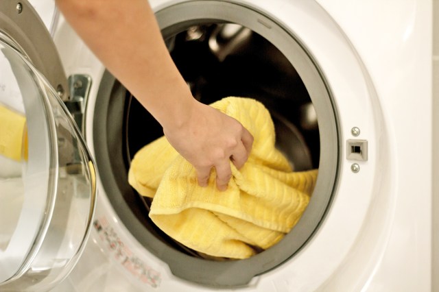 Anonymous woman putting a yellow towel into a white front-loading dryer.