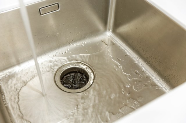 Close up of a garbage disposal drain in a stainless steel sink with the water running.