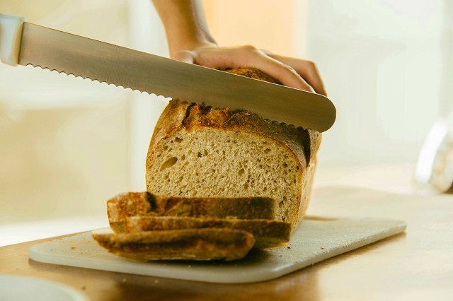 Anonymous person using a long serrated knife to slice a loaf of bread.