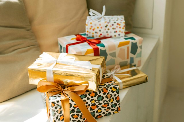 A pile of five beautifully wrapped presents with bows and different types of wrapping paper. They're perched on a ledge next to some throw pillows.