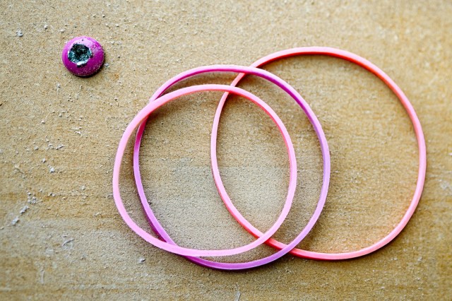 Three wide rubber bands on a piece of wood next to a screw that appears to be stripped.