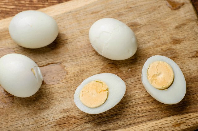 Three whole peeled hard-boiled eggs on a wooden cutting board, plus two halves with the hardened yokes facing upward.