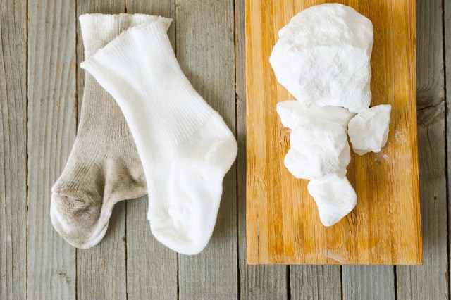 A wooden surface with one dingy sock and one bright white sock. Sitting next to them are a few clumps of sodium percarbonate.