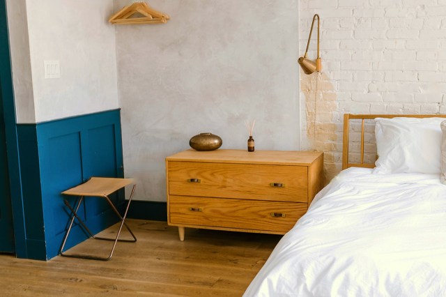 A white and blue bedroom with a wooden bed next to a matching wood nightstand with two large drawers for storage.