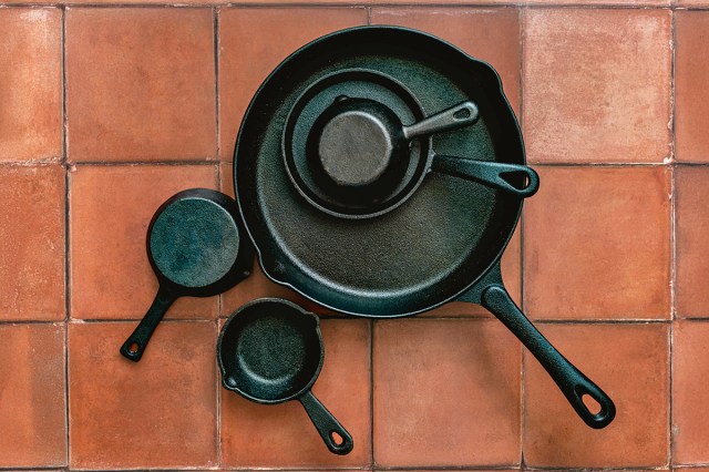 Five different-sized cast-iron skillets — some stacked on top of each other — on a terracotta tile surface, seen from above.