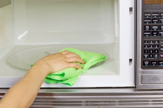 Anonymous person using a green microfiber cloth to clean the inside of a microwave.