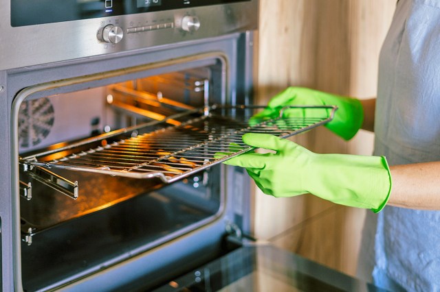 Anonymous person wearing bright green cleaning gloves removing one of the metal racks from an oven.