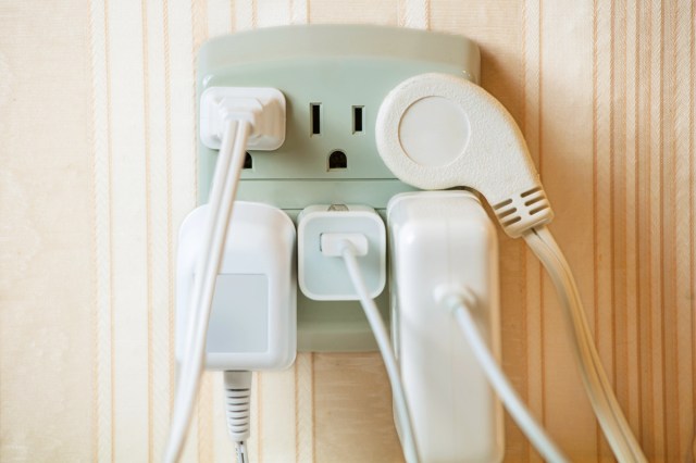 A power strip mounted to a wall outlet with five different devices plugged into it.