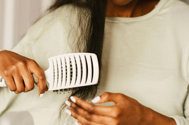 Anonymous woman wearing an off-white sweatshirt brushing her long hair with a white, flat hair brush.