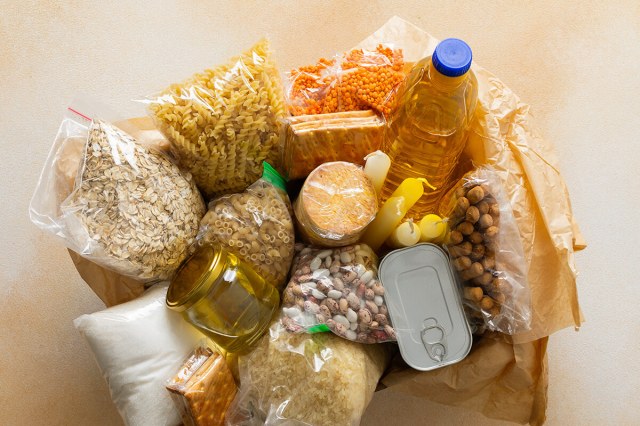 An overhead shot of bagged pantry goods including oats, pasta, nuts, rice, and lentils, plus a couple of cans and a bottle of cooking oil.