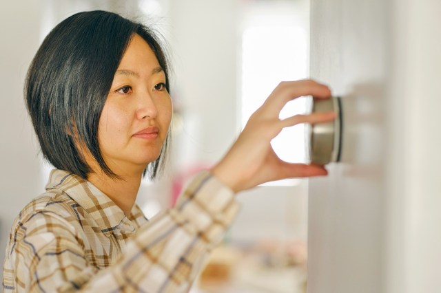 A middle-aged woman with a bob haircut adjusting a smart thermostat on the wall.