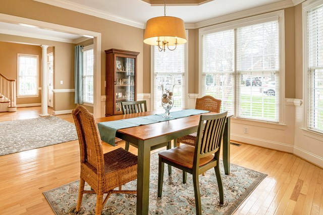 A small dining room with a wooden table and a chair on each side. Over the table is a chandelier, and under it is an area rug.