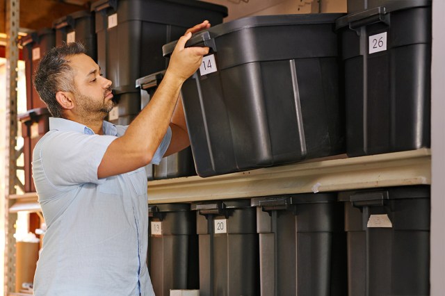 A man removing a numbered storage bin from a shelving unit in a garage.