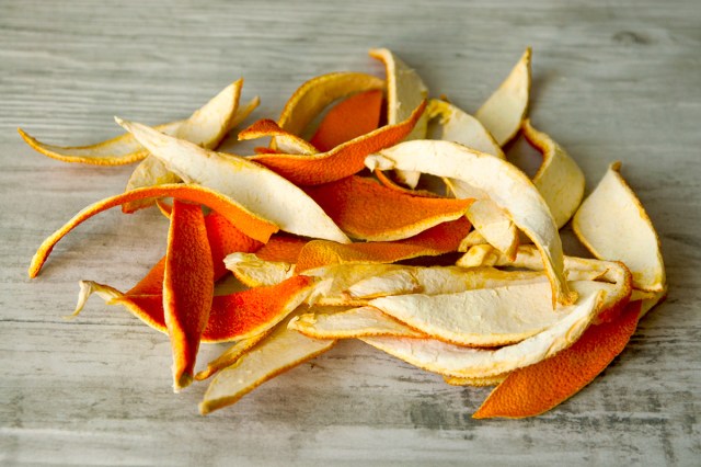 A pile of orange peels on a grayish wood surface.