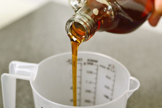 Anonymous person pouring maple syrup into a plastic measuring container.