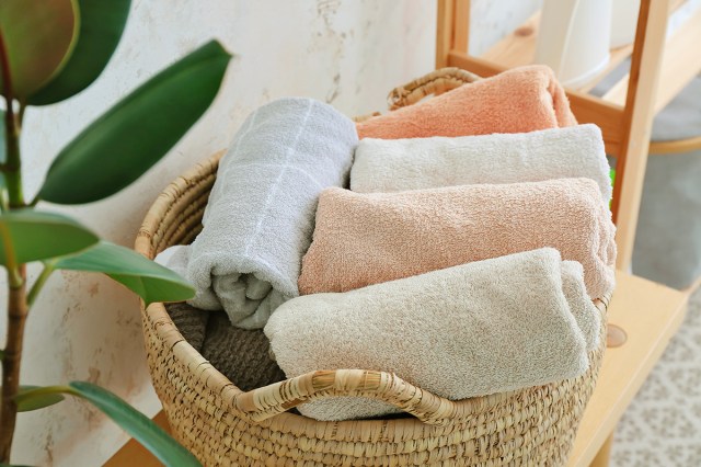 A woven basket full of rolled-up bath towels on a bench next to a plant.
