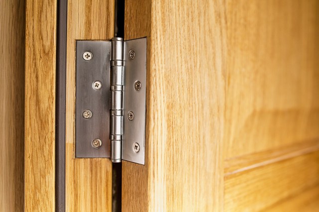 A close-up of a hinge on a wooden interior door.