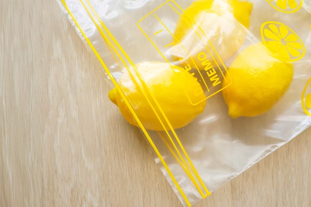 Lemons in a resealable plastic bag that's open on a wood countertop.