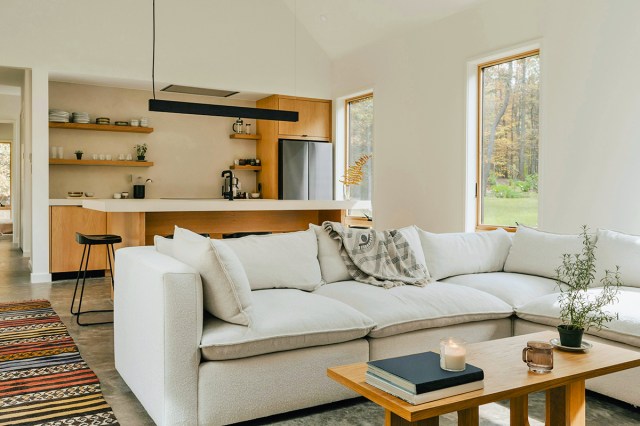 An open-concept kitchen and living room with an oversized, off-white sectional in the foreground and a wooden, stone-topped kitchen island in the background.