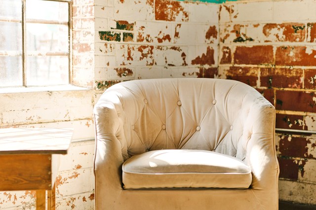 An off-white, vintage-looking swivel chair against an exposed brick wall with peeling off-white paint.