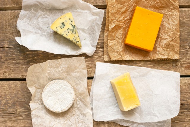 Four different types of cheeses on wrapping paper. It's shot from above and the wrappers are on a slatted wood table.