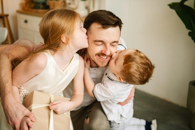 A dad getting kissed on either cheek by his two young children.