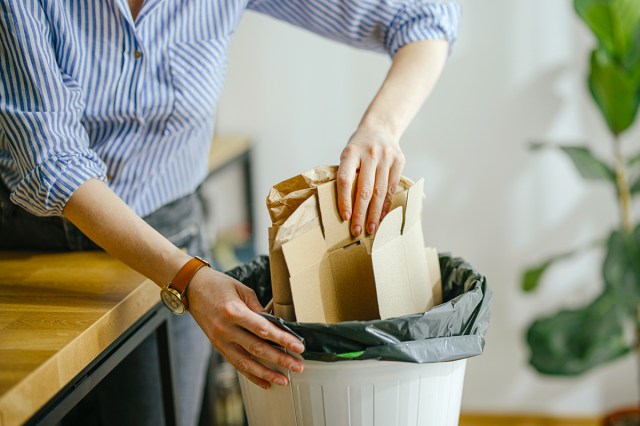 Anonymous person putting empty, folded-flat boxes into a garbage can.