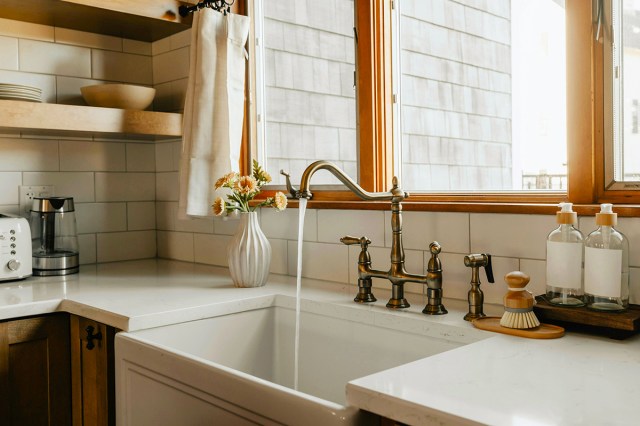 Water flowing out of a newer-looking bridge faucet in a stylish kitchen.