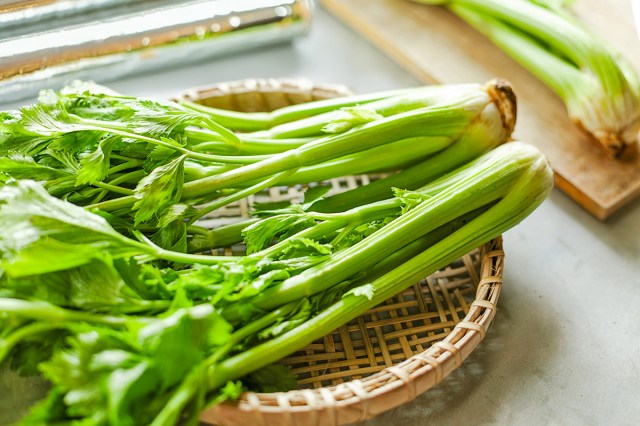Close-up of two stalks of celery on a round, woven rattan serving plate.