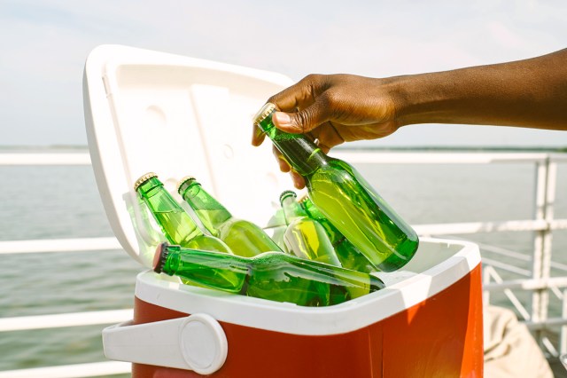 Anonymous person reaching into a red and white cooler that appears to be on a boat as you can see the railing and the water.