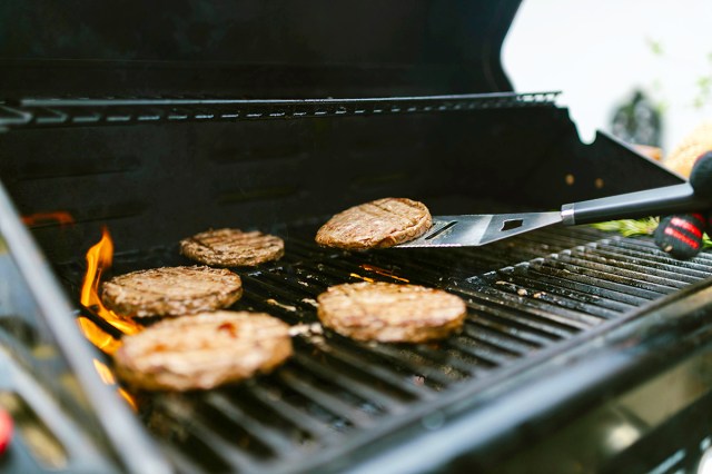 Close-up of anonymous person flipping burgers on a grill using a turner.