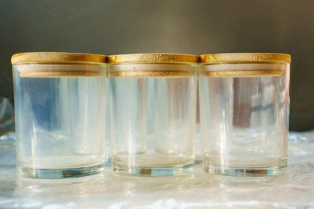 Three identical, empty clear glass candle jars with wooden lids.