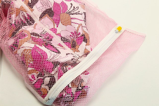 A pink floral swimsuit in a pink mesh bag with a white zipper and a yellow pull against an off-white background.