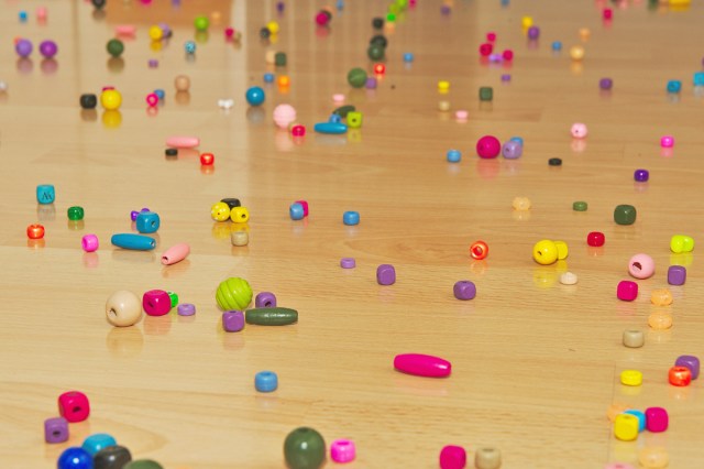 A light-colored wood floor with multicolored beads in various shapes scattered across it.