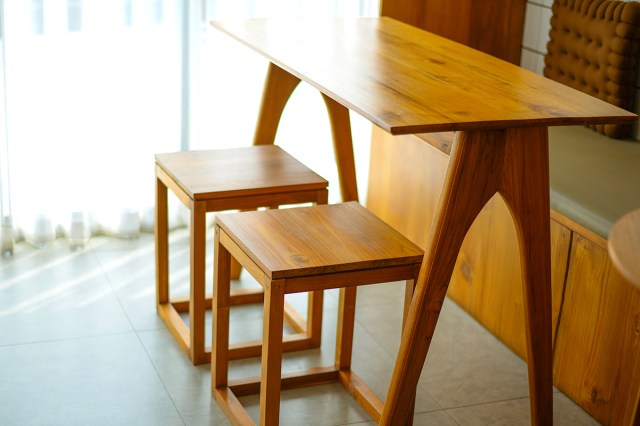 A small wooden table with long geometric legs and two matching wood stools.