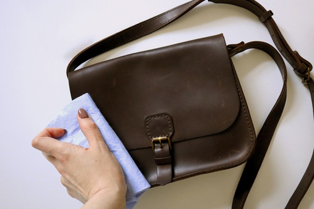 Anonymous person using a microfiber cloth to clean a vintage brown leather handbag.