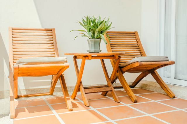 Two teak lounge chairs on an outdoor patio with terracotta tile. Between the chairs is a small teak folding table with a potted plant on top of it.